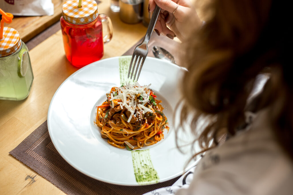 side view a girl eats spaghetti with meat and grated cheese